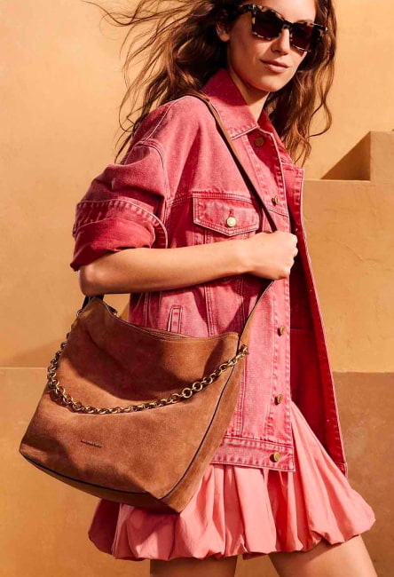 Mujer usando chamarra de mezclilla rosa y bolso de hombro color caf&eacute; Michael Kors